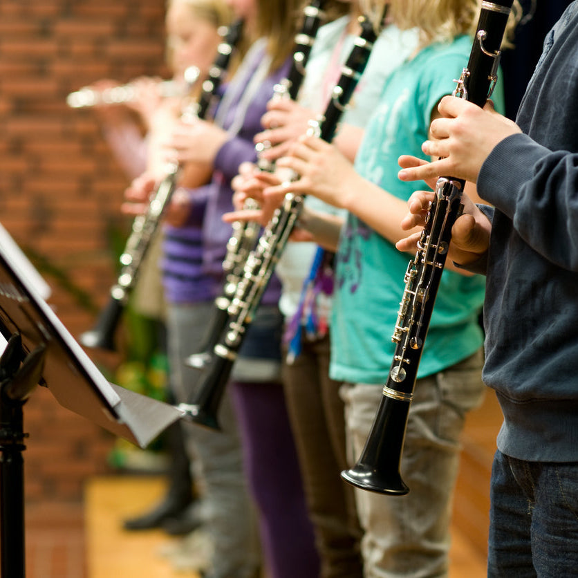 Children playing clarinets in a music class with sheet music stands.