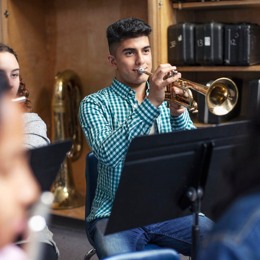 Person playing a trumpet in a band setting with musical instruments in the background.